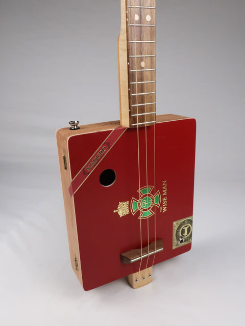 Tilted front view of a cigar box guitar handmade by Mike Snowden. This red 3 string cigar box guitar has a walnut fretboard and maple neck.