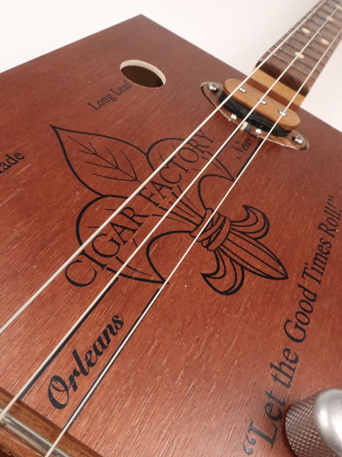 Front tilted view of a 3 string cigar box guitar handmade by Mike Snowden of Snowden Guitars. This CBG is made with a New Orleans Cigar Factory cigar box.