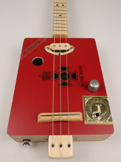 Front view of The Wise Man 3 string cigar box guitar handmade by Mike Snowden. This cigar box is made with a red cigar box with The Wise Man printed on the front.