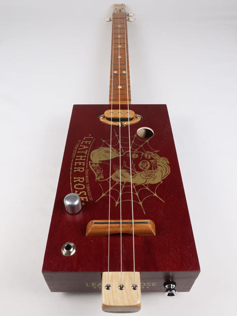 Front view of a Leather Rose 3 string cigar box guitar. Red painted cigar box with gold Leather Rose graphic on the front. This cigar box guitar is handmade by Mike Snowden of Snowden Guitars.