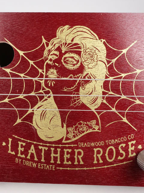 Close up front view of a Leather Rose 3 string cigar box guitar. Red painted cigar box with gold Leather Rose graphic on the front. This cigar box guitar is handmade by Mike Snowden of Snowden Guitars.
