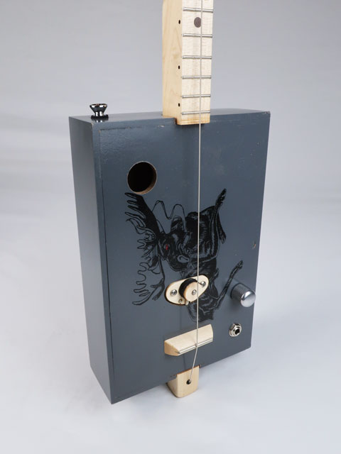Tilted front view of a one string diddly bow cigar box guitar with a moose on the front. This cigar box guitar is handmade by Mike Snowden and had a maple single coil pickup.