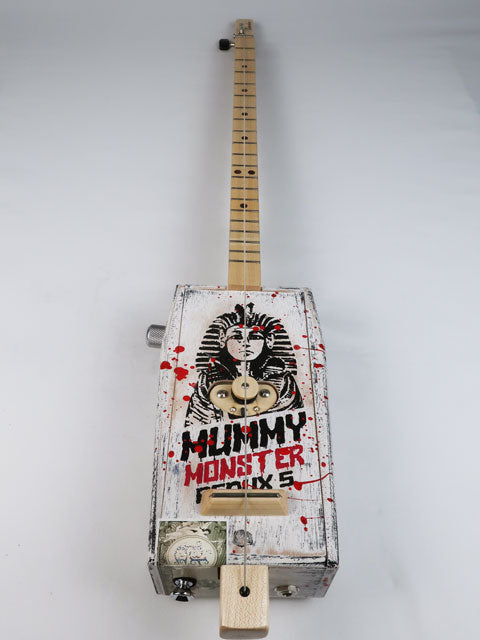 Front view of a cigar box guitar made from a coffin shaped Mummy Monster cigar box. This one string diddly bow is handmade by Mike Snowden and as an Egyptian Pharos on the front. 