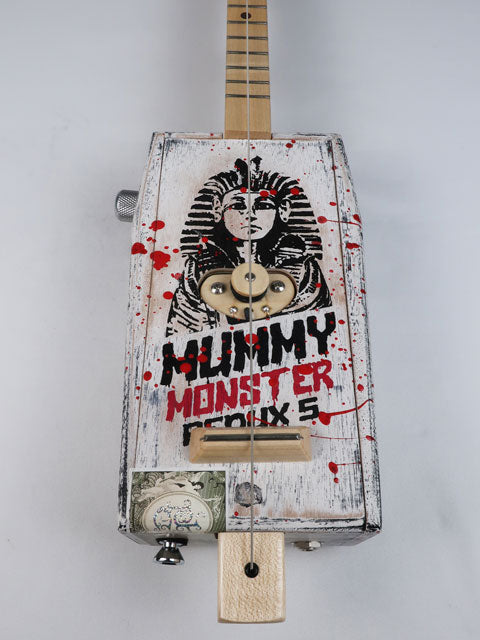 Front view of a cigar box guitar made from a coffin shaped Mummy Monster cigar box. This one string diddly bow is handmade by Mike Snowden and as an Egyptian Pharos on the front. 