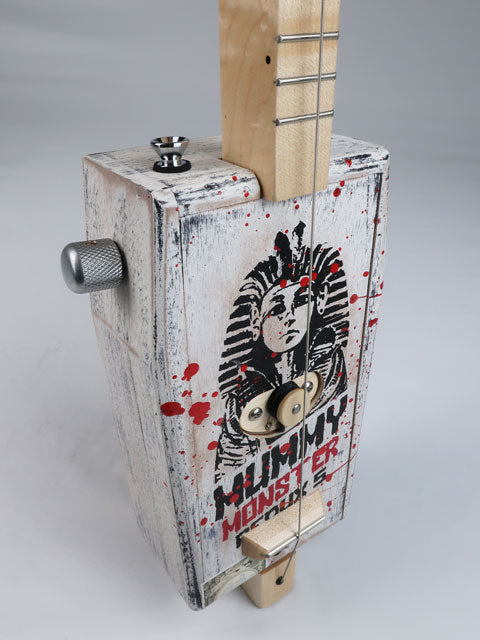 Front view of a cigar box guitar side volume knob made from a coffin shaped Mummy Monster cigar box. This one string diddly bow is handmade by Mike Snowden and as an Egyptian Pharos on the front. 