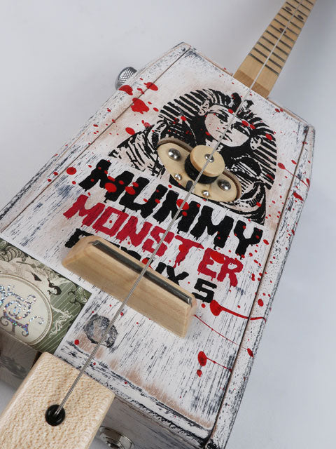 Tiled front view of a cigar box guitar made from a coffin shaped Mummy Monster cigar box. This one string diddly bow is handmade by Mike Snowden and as an Egyptian Pharos on the front. 