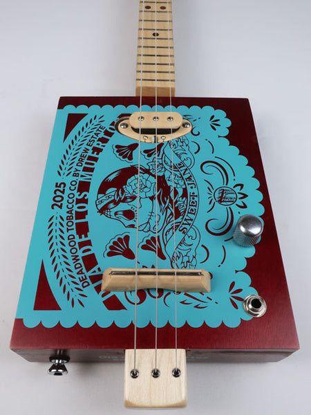 Front view of a 3 string cigar box guitar with Sweet Jane logo printed in teal on a red cigar box. This cigar box guitar has a maple neck and maple single coil pickup and is handmade by Mike Snowden of Snowden Guitars.