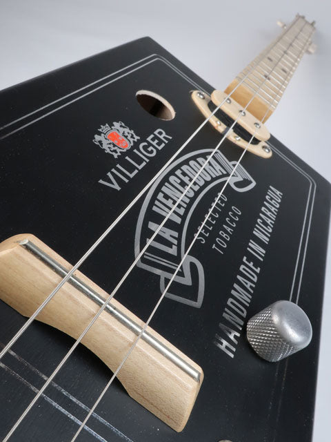 Tilted view Front of a 3 string cigar box guitar with a maple single coil pickup. Villigaer La Vencedora logo printed in silver on a black cigar box. This cigar box guitar is handmade by Mike Snowden.