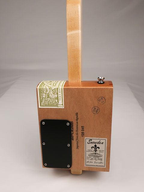Back view of a cigar box guitar handmade by Mike Snowden of Snowden Guitars. There is a stick on the back of the cigar box guitar with the date and number of guitars made. 
